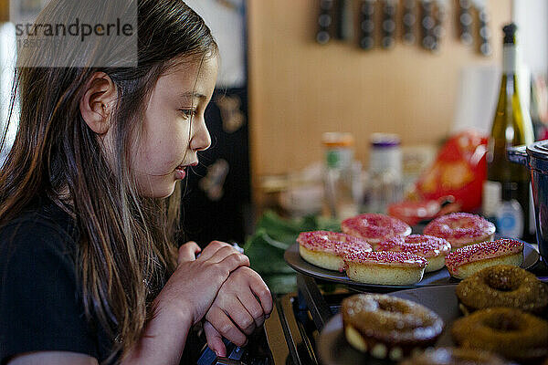 Ein kleines Mädchen starrt sehnsüchtig auf Donuts auf der Arbeitsplatte