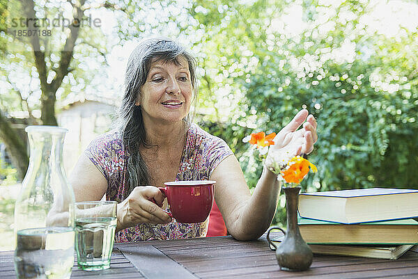 Ältere Frau trinkt Kaffee und betrachtet frische Blumenvasen im Garten  Altötting  Bayern  Deutschland
