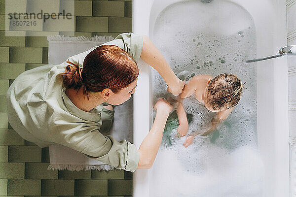 Frau badet ein kleines glückliches Mädchen im Badezimmer mit Schaum
