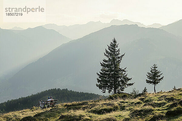 Ein Paar Mountainbiker blickt auf die Aussicht und sitzt auf einer Bank in der alpinen Landschaft  Zillertal  Tirol  Österreich