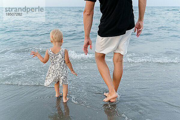 Ein Mann mit einem Mädchen an der Hand steht am Meeresufer  Rückansicht