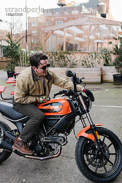 Mann auf orange-schwarzem Motorrad parkt im Innenhof