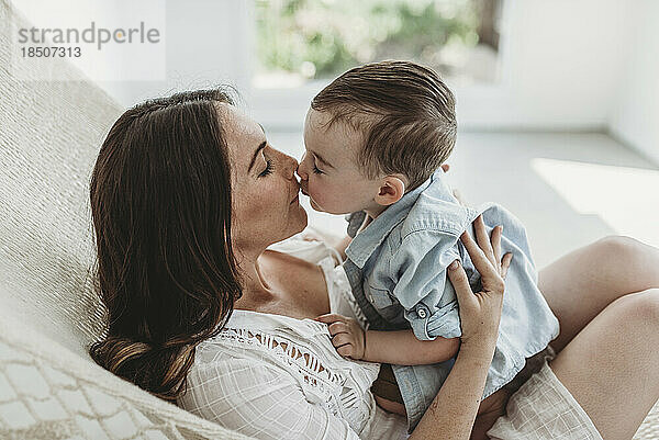 Mutter und Sohn küssen und kuscheln in der Hängematte im Studio mit natürlichem Licht