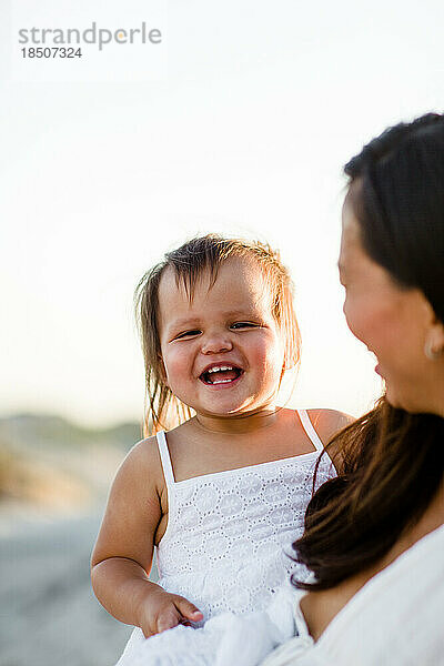 Mutter hält lachendes Kleinkind am Coronado Beach in San Diego