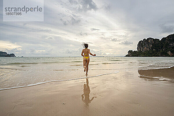 Frau im gelben Bikini läuft bei Sonnenuntergang am Railay Beach.