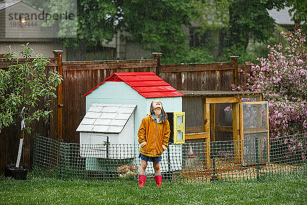 Ein glückliches Mädchen steht im Regen neben dem Hühnerstall und blickt nach oben