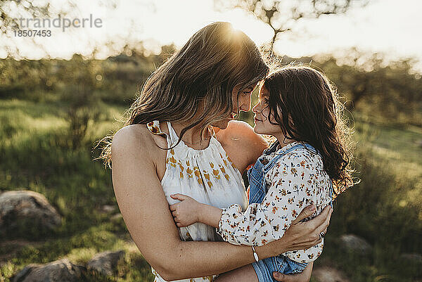 Junge Mutter hält Tochter und kuschelt im hellen kalifornischen Feld