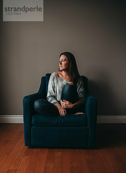 Attraktive Frau sitzt in einem bequemen Stuhl in einem leeren Raum.