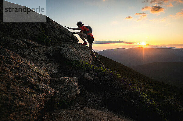 Silhouette eines Trailrunner-Mannes  der bei Sonnenaufgang in Felsen klettert
