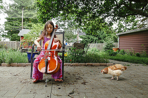 Ein kleines Kind spielt draußen Cello für sein Haustierhuhn