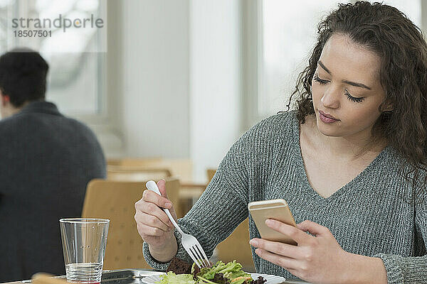 Student isst in der Kantine Salat und telefoniert mit dem Handy. Schule  Bayern  Deutschland