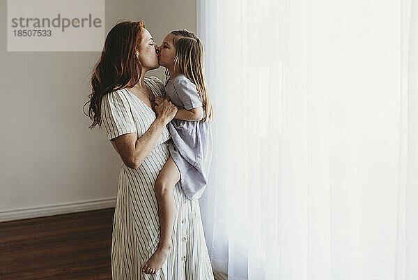 Seitenansicht einer jungen Mutter  die ihre Tochter hält und im Studio küsst