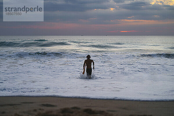 Mann-Surfer mit einem Surfbrett im Meer bei Sonnenuntergang.