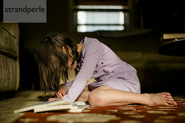 Ein kleines Kind sitzt im Morgenlicht auf einem Teppich und liest einen Stapel Bücher