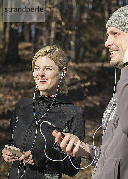 Mann und Frau in Sportkleidung hören im Wald Musik auf dem Smartphone