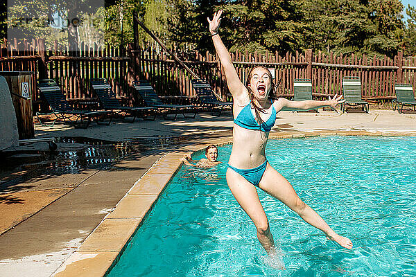 Teenager-Mädchen springt an sonnigem Tag in den Pool