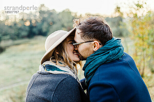 Ein Mann und eine Frau in Mänteln küssen sich im Park bei einem Date