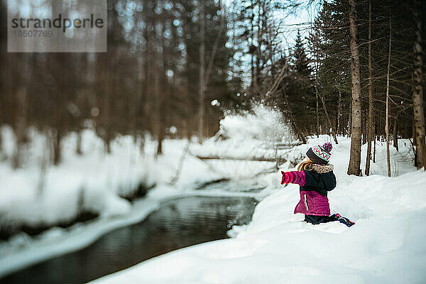 Mädchen wirft an einem Wintertag Schnee in einen Fluss