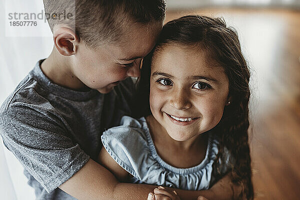 Portrait of young girl while brother embraces her and laughs