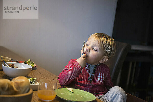 Kleiner Junge leckt sich am Frühstückstisch den Finger  München  Deutschland