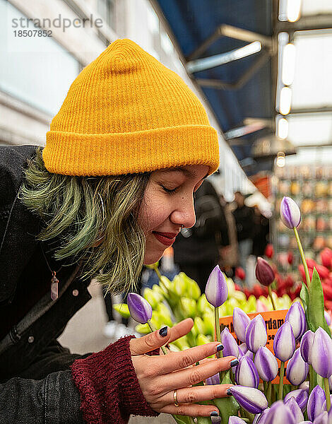 Frau mit gelbem Hut riecht beim Einkaufen im Floristen an Tulpenblüten.