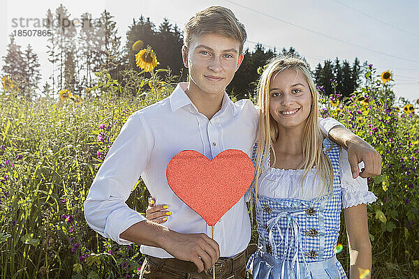 Teenager-Paar mit Herzform vor Sonnenblumenfeld  Bayern  Deutschland