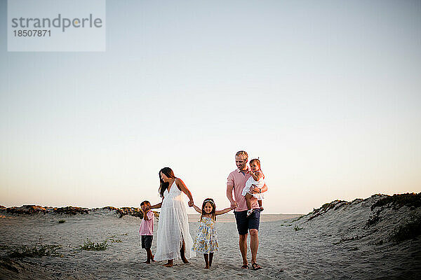 Fünfköpfige Familie hält Händchen und geht am Coronado Beach in San Diego spazieren