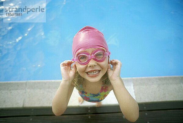 Ein kleines Mädchen am Pool lächelt in die Kamera.