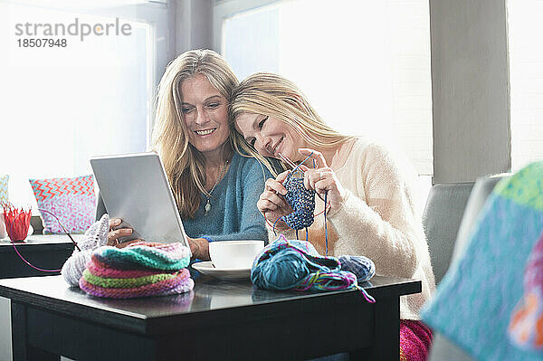 Zwei Frauen stricken Schalldämpfer und benutzen ein digitales Tablet im Café und lächeln  Bayern  Deutschland