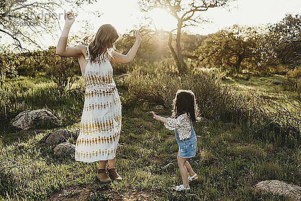 Junge Mutter und Tochter tanzen im Sonnenlicht im hellen Feld