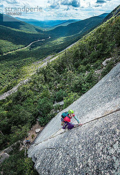 Mann klettert steilen Riss an der Felswand mit Tal dahinter