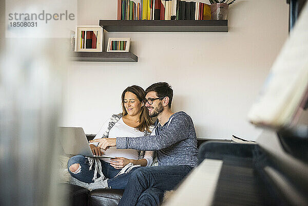 Schwangere Frau und Ehemann mit Laptop auf Sofa  München  Deutschland