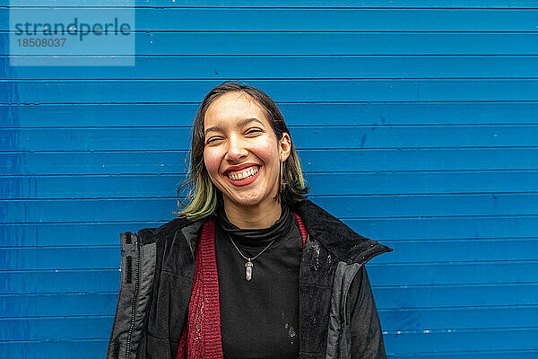 Glückliche Frau steht im Regen auf der Straße  in der Nähe der blauen Wand.
