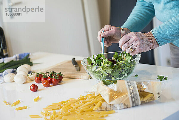 Alte Frau mischt Salat auf dem Küchentisch