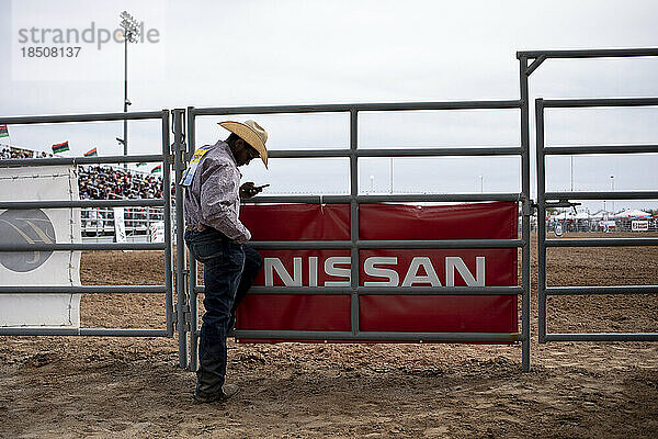 Ein Cowboy überprüft sein Telefon beim Arizona Black Rodeo