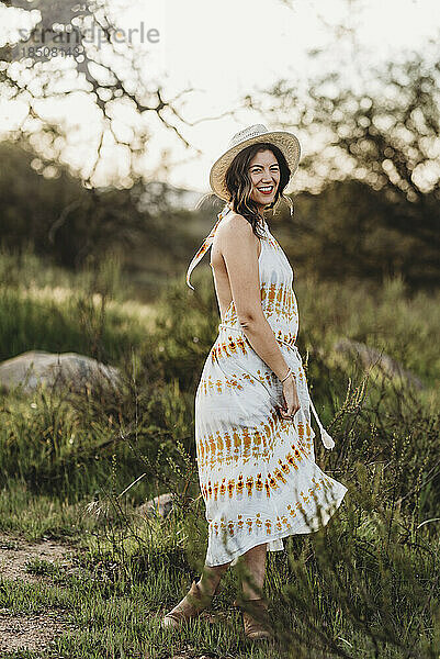 Ganzkörperporträt einer lächelnden jungen Frau im Kleid im Hintergrundbeleuchtungsfeld