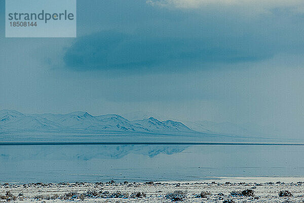 Berge spiegeln sich im Winter auf einem zugefrorenen See.