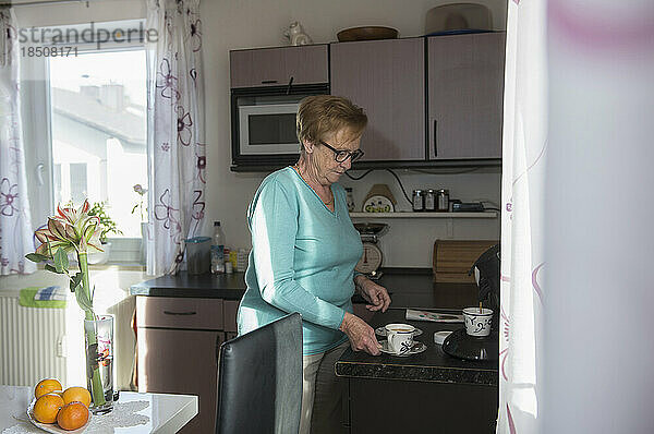 Ältere Frau trinkt eine Tasse Kaffee von der Küchentheke