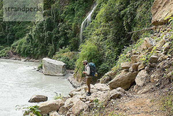 Junger Mann wandert in den Bergen entlang eines Flusses mit Wasserfall