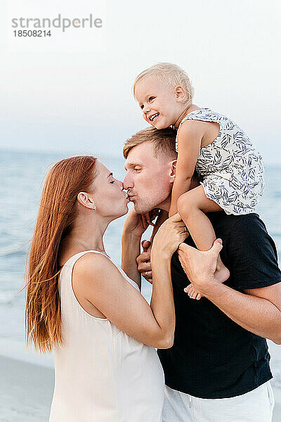 Seitenansicht einer glücklichen Familie mit einem kleinen Kind  das sich am Strand umarmt