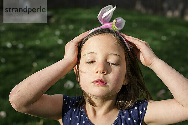 Ein wunderschönes kleines Mädchen mit ernstem Gesichtsausdruck trägt eine Blume als Hut
