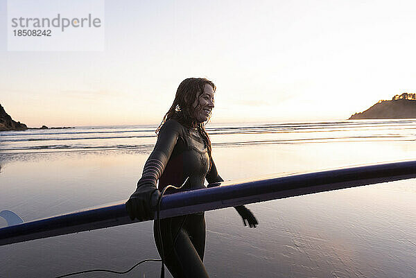Frau trägt Surfbrett entlang der Küste von Oregon