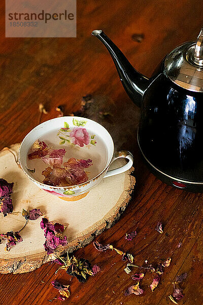Schwarzer Teekessel neben einer Teetasse mit rosa Blüten