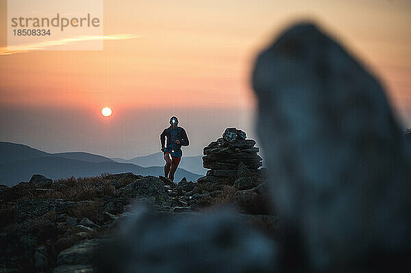 Silhouette männlicher Trailrunner  die bei Sonnenaufgang auf einem felsigen Pfad laufen