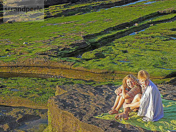 Junge Freunde picknicken am felsigen Strand von Playa de Azkorri  Getxo  Baskenland  Spanien