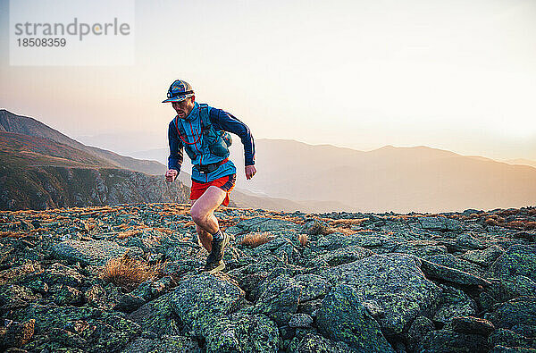 Männlicher Trailrunner läuft bei Sonnenaufgang in den Bergen über Felsen