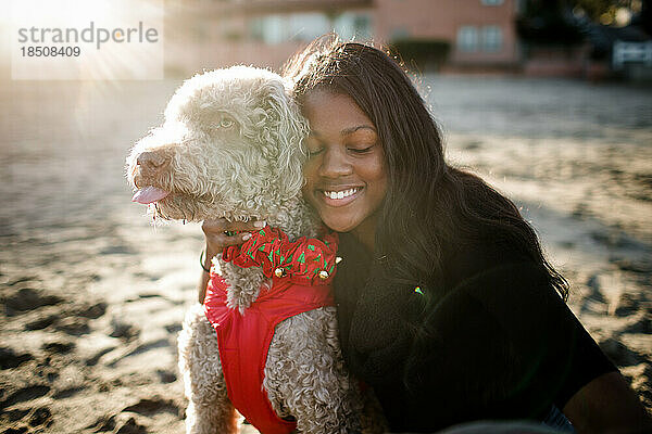 Young girl hugging labradoodle on beach at sunset