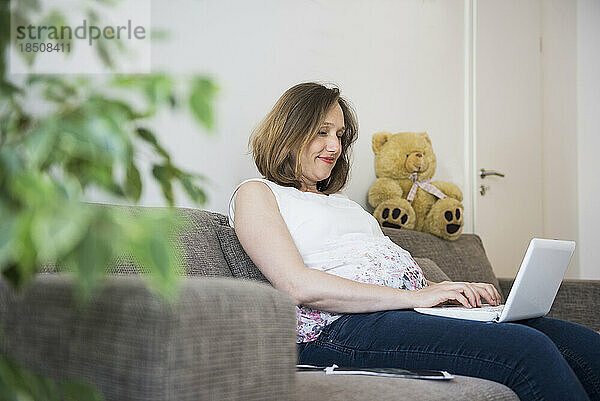 Schwangere Frau sitzt auf Sofa und arbeitet am Laptop  München  Bayern  Deutschland