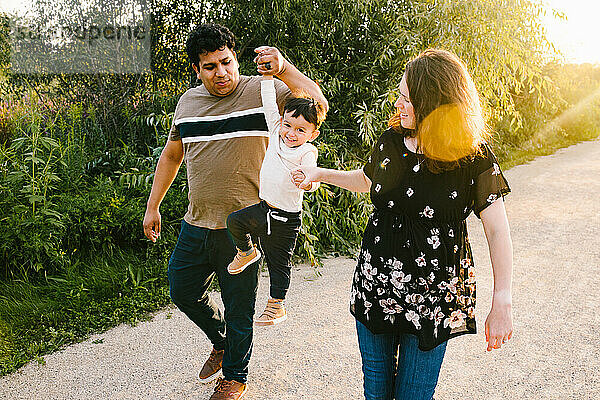 Schwangere Mutter und Latino-Vater lächeln und spielen mit ihrem Sohn im Sonnenschein