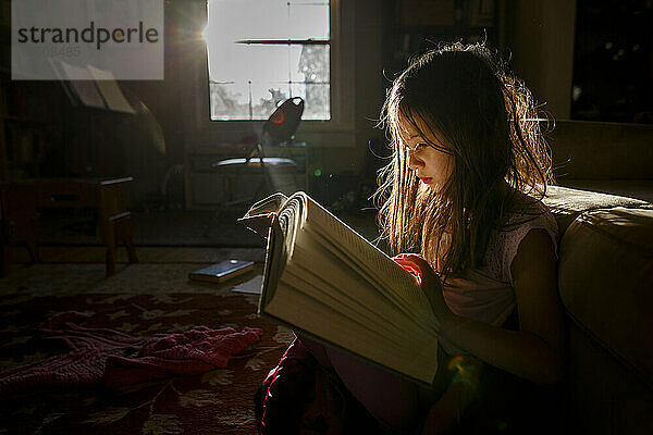 Ein kleines Kind sitzt im hellen Sonnenlicht und liest ein großes Buch